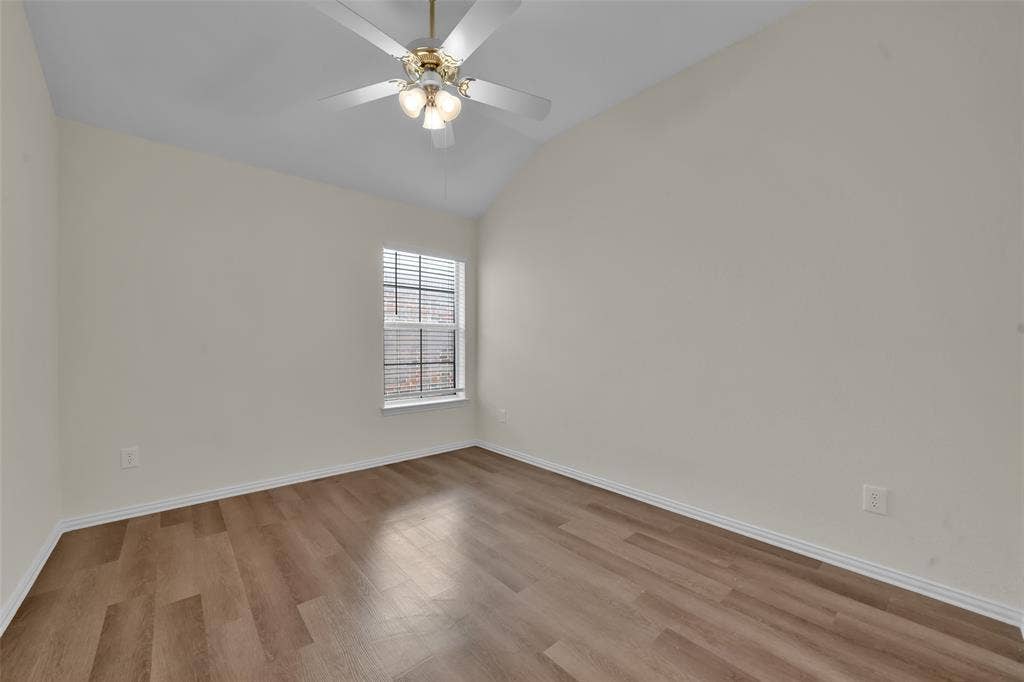 Vaulted ceiling with a ceiling fan, window with blinds, wood-finish flooring, and light-colored walls