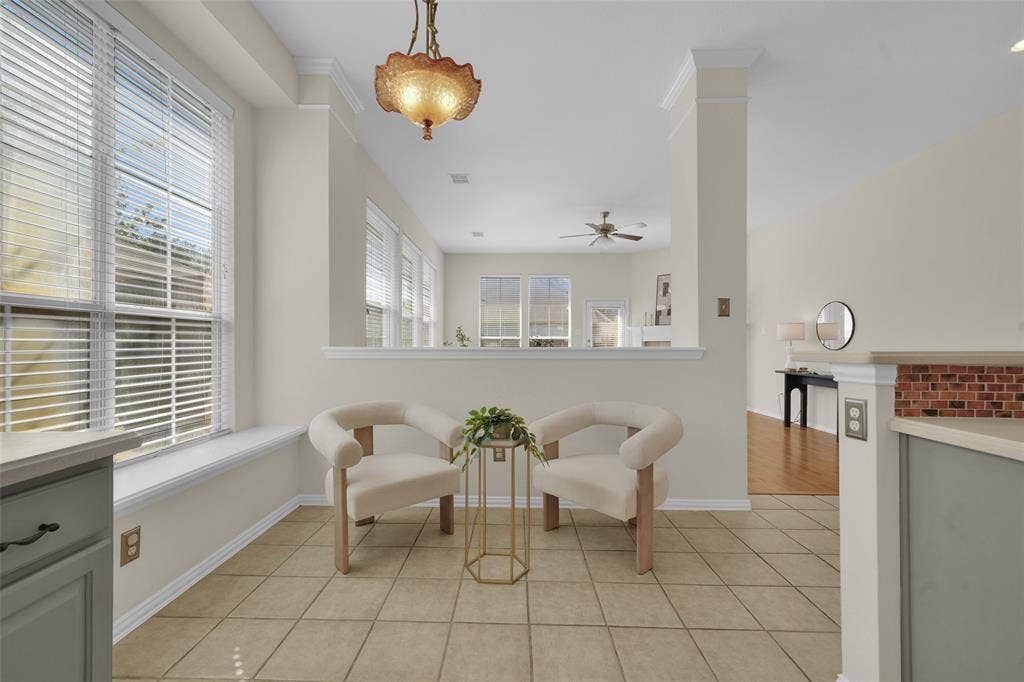 Tiled flooring with a warm finish, multiple windows with blinds, architectural half-wall with brick-finish detailing, and an ornate ceiling fixture