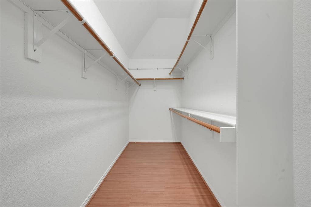 Walk-in closet with wood-finish flooring, white walls, and multiple levels of shelving and hanging rods