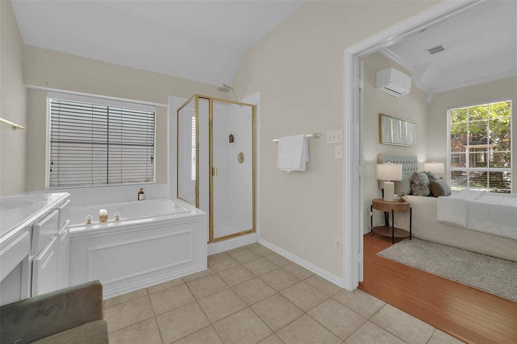Soaking tub with a window, glass-enclosed shower with gold-toned fixtures, and a white vanity with integrated sink