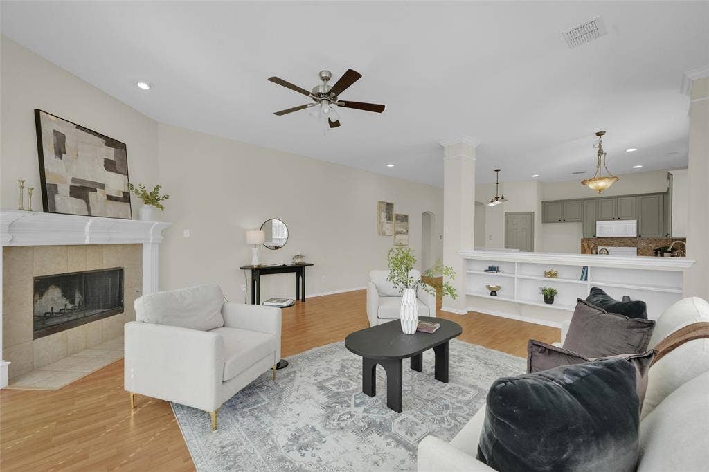 Vaulted ceiling with a ceiling fan, recessed lighting, tile-surround fireplace with a mantel, wood-finish flooring, and built-in shelving