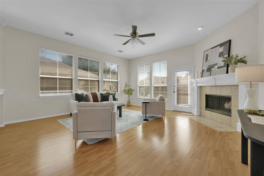 Bright living space featuring wood-finish flooring, multiple windows, a ceiling fan, and a fireplace with a tile surround and mantel
