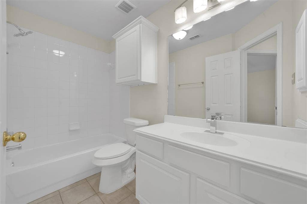 White tiled shower and tub combination, white vanity with integrated sink, chrome faucet, and overhead cabinet storage