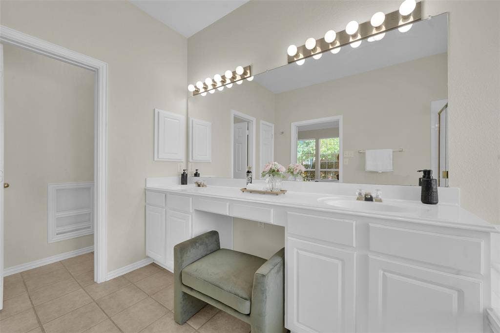 Dual vanity with white cabinetry, integrated sinks, white countertops, and a full-width mirror with overhead theatrical lighting