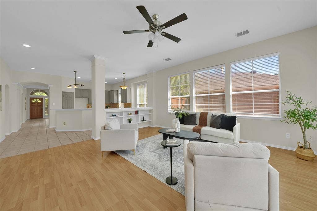 Living area with wood-finish flooring, built-in shelving, a ceiling fan, and multiple windows