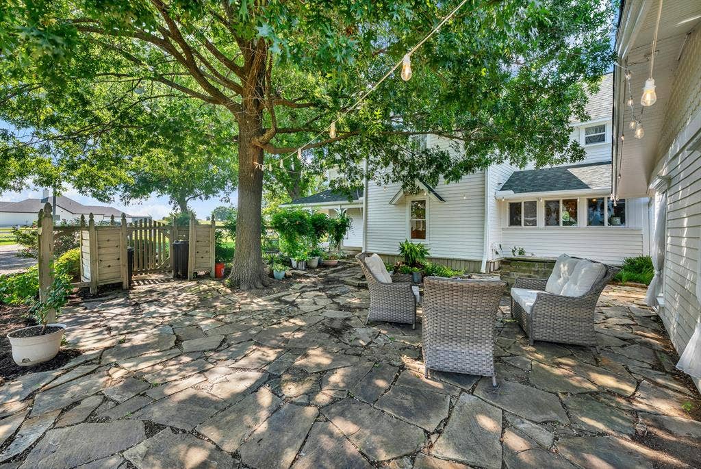 1425-1 Lone Star Road, Celina, TX 75009 A charming flagstone courtyard creates a peaceful outdoor retreat beneath the shade of mature oak trees. String lighting, lush landscaping, and ample seating provide the perfect setting for morning coffee, quiet evenings, or entertaining guests.