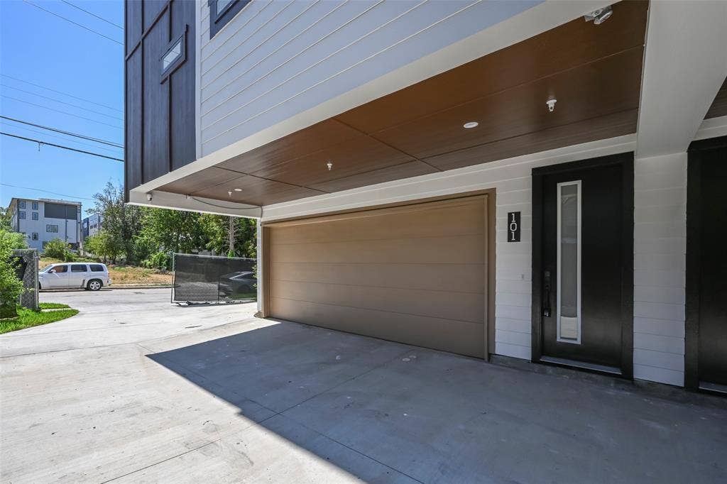 2247 Mail Avenue, #102, Dallas, TX 75235 Concrete driveway with a covered entry, featuring a brown garage door, dark entry door with vertical window, and light gray siding