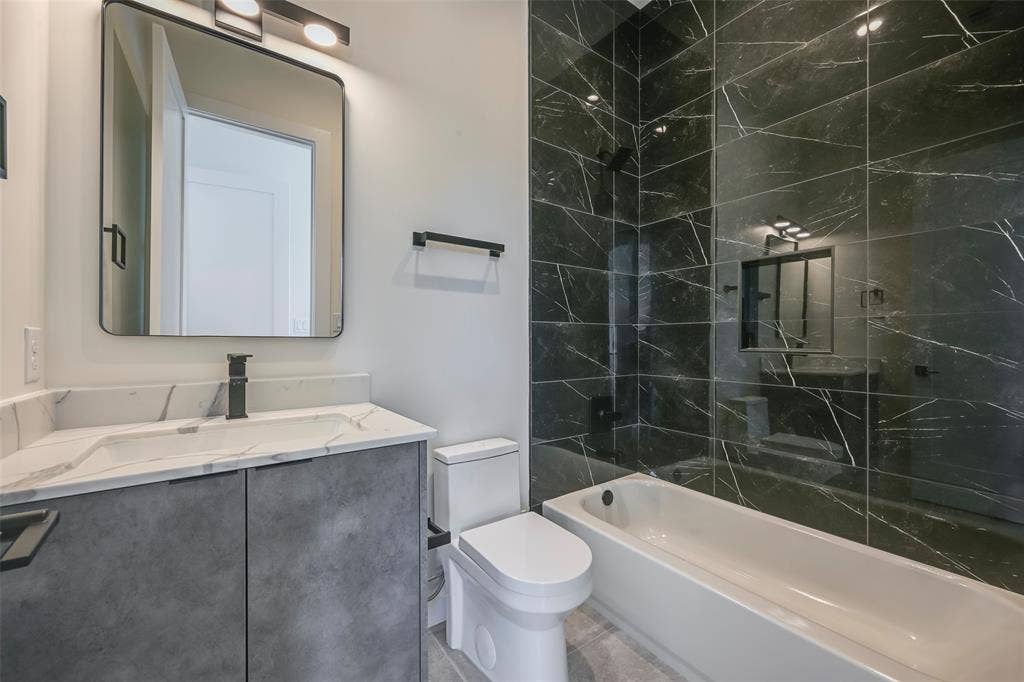 2247 Mail Avenue, #101, Dallas, TX 75235 Vanity with integrated sink and matte black faucet, framed mirror with overhead lighting, black tiled shower with built-in niche, and white bathtub