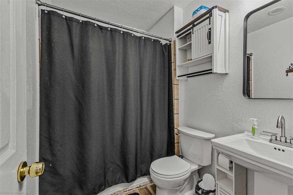 Bathroom featuring a pedestal sink with a metallic faucet, a wall-mounted medicine cabinet with sliding barn-style door, and a shower area with a metal tension rod
