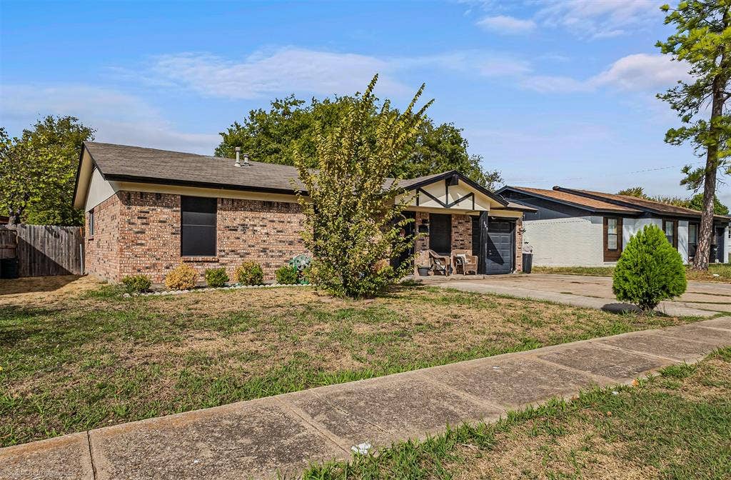 Single-story exterior featuring a brick facade, gable roofline, decorative timbering details, and a concrete driveway