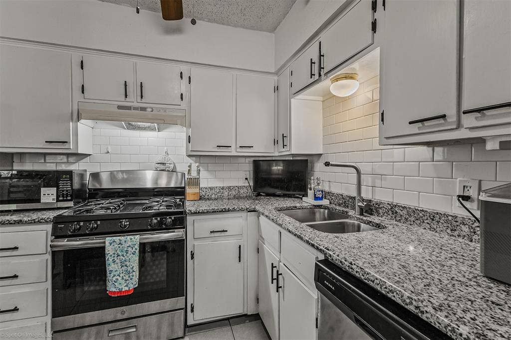 Kitchen featuring white cabinetry with matte black hardware, stone-finish countertops, white subway tile backsplash, and stainless steel appliances