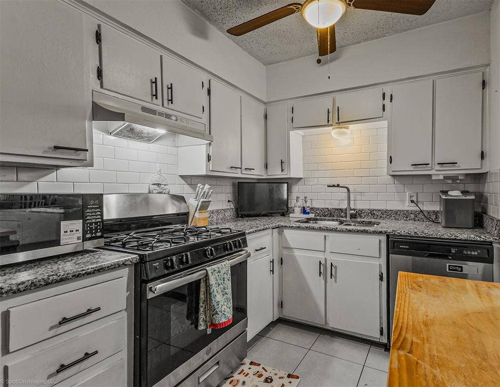 Kitchen featuring stone countertops, white cabinetry with matte black hardware, subway tile backsplash, stainless steel gas range, and tile flooring