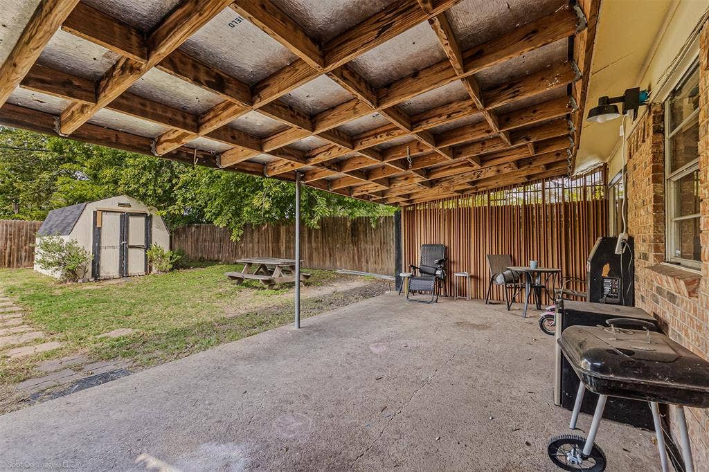 Covered patio featuring an exposed timber-beam ceiling, concrete flooring, and a vertical wood-slat privacy screen