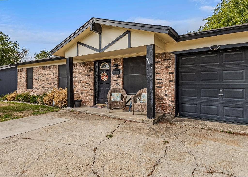 Single-story brick exterior featuring a covered front porch, dark-finished timber support beams, and a built-in single-car garage