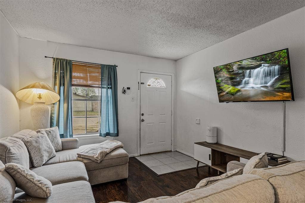 Interior space featuring wood-finish flooring, a multi-pane window with natural light exposure, and a single-panel entry door with an arched decorative glass insert and tiled entryway flooring