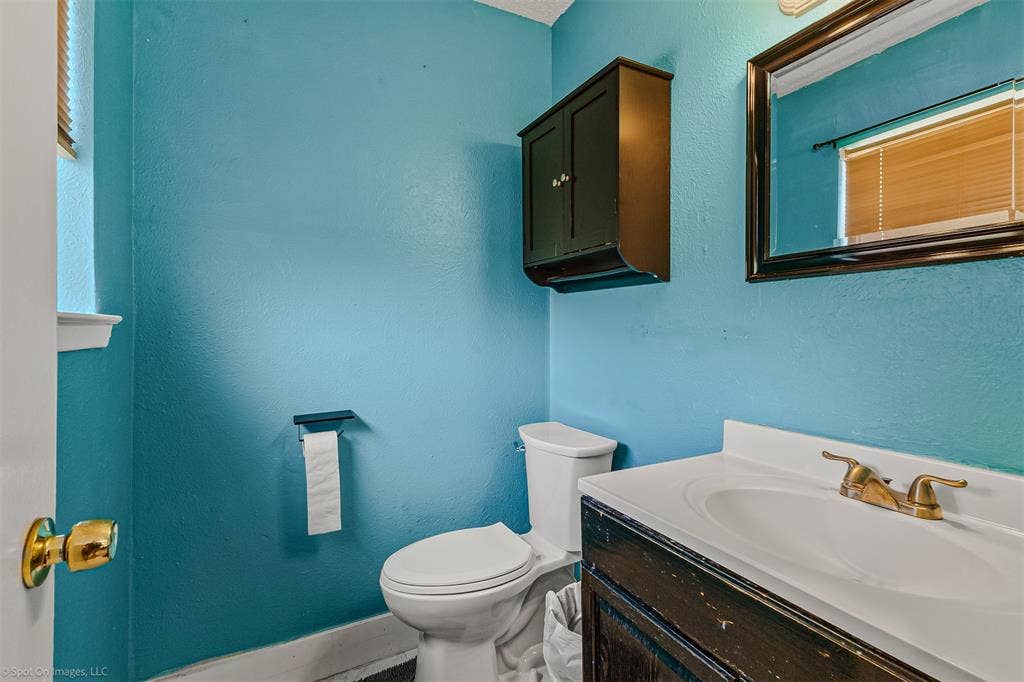 Bathroom featuring a vanity with an integrated countertop sink, wall-mounted storage cabinet, framed mirror, and two-piece toilet