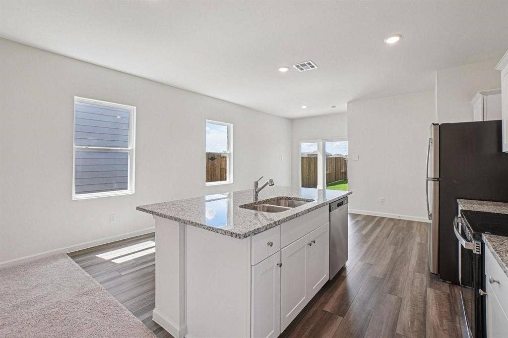6053 Mojave Drive, Forney, TX 75126 Kitchen island with a double basin sink, stainless steel appliances, white cabinetry, granite countertops, and wood-finish flooring
