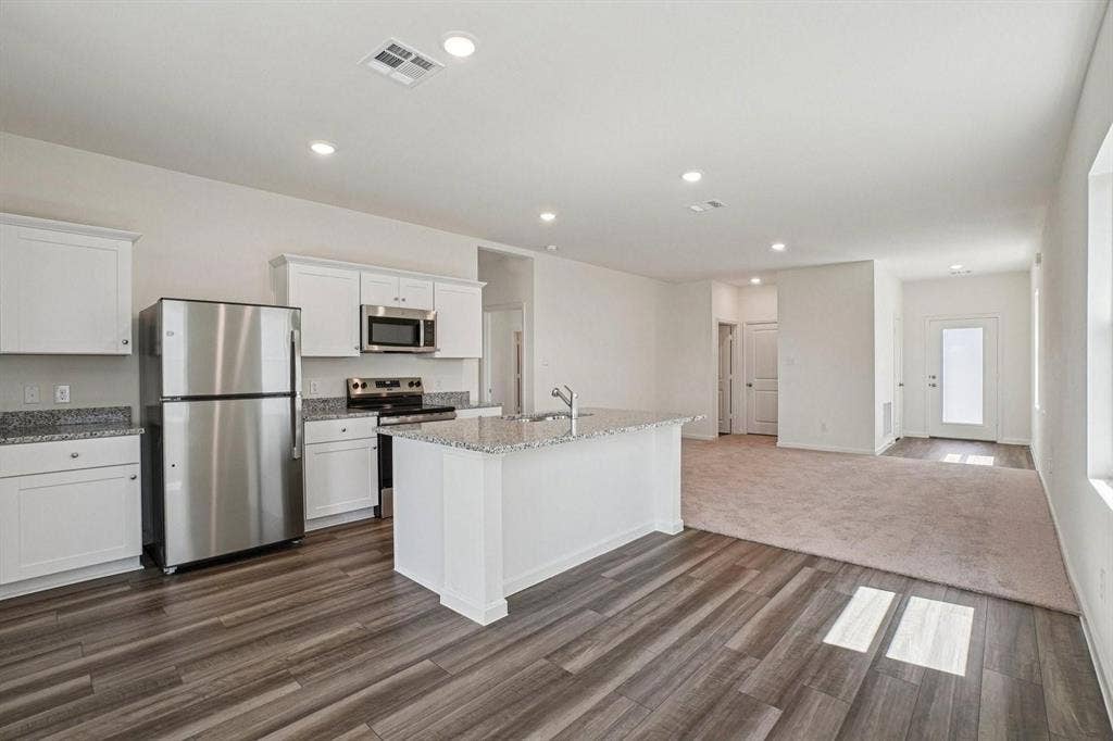 6053 Mojave Drive, Forney, TX 75126 Open-concept living space featuring a kitchen island with a built-in sink, stainless steel appliances, white cabinetry, and granite countertops