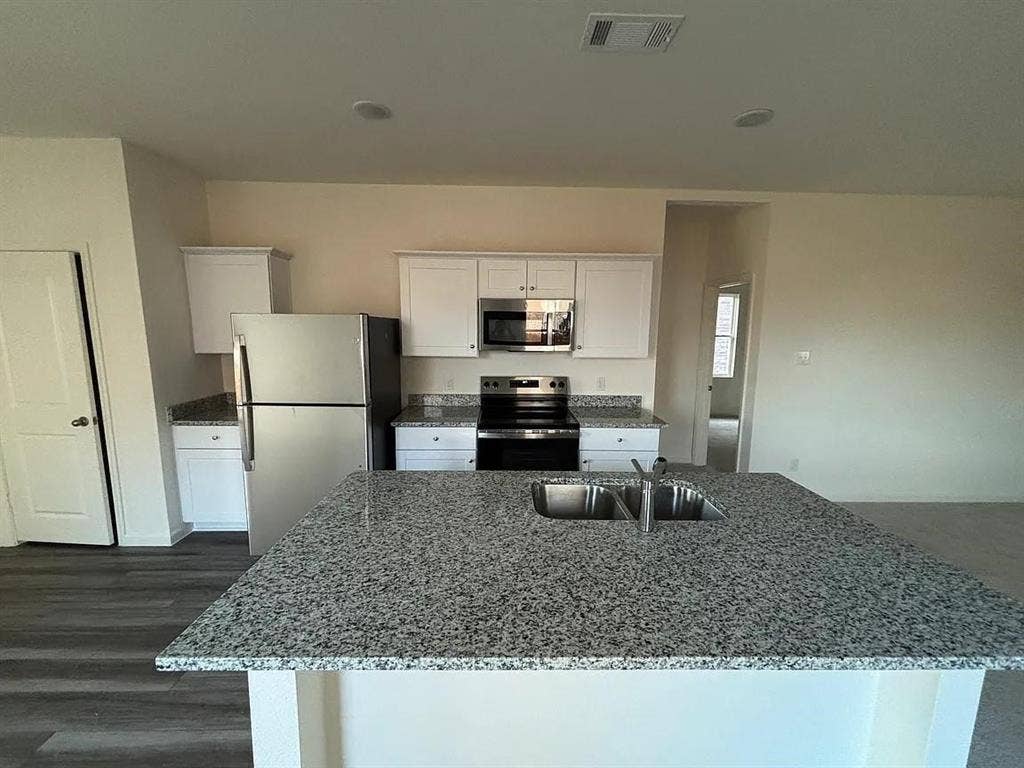 5944 Sahara Drive, Forney, TX 75126 Kitchen featuring an island with a dual basin sink, stone-finish countertops, white cabinetry, wood-finish flooring, and stainless steel appliances