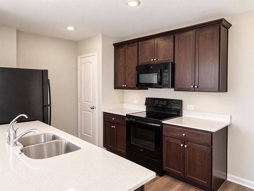 9226 Summerlee Street, Dallas, TX 75227 Kitchen featuring dark wood-finish cabinetry, light-toned countertops, a double basin stainless steel sink, and black appliances