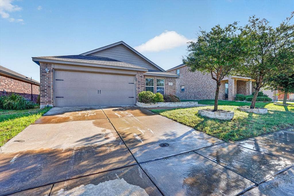 2428 Rosharon Drive, Forney, TX 75126 Brick veneer exterior with a two-car garage, concrete driveway, and established landscaping with stone-edged planters