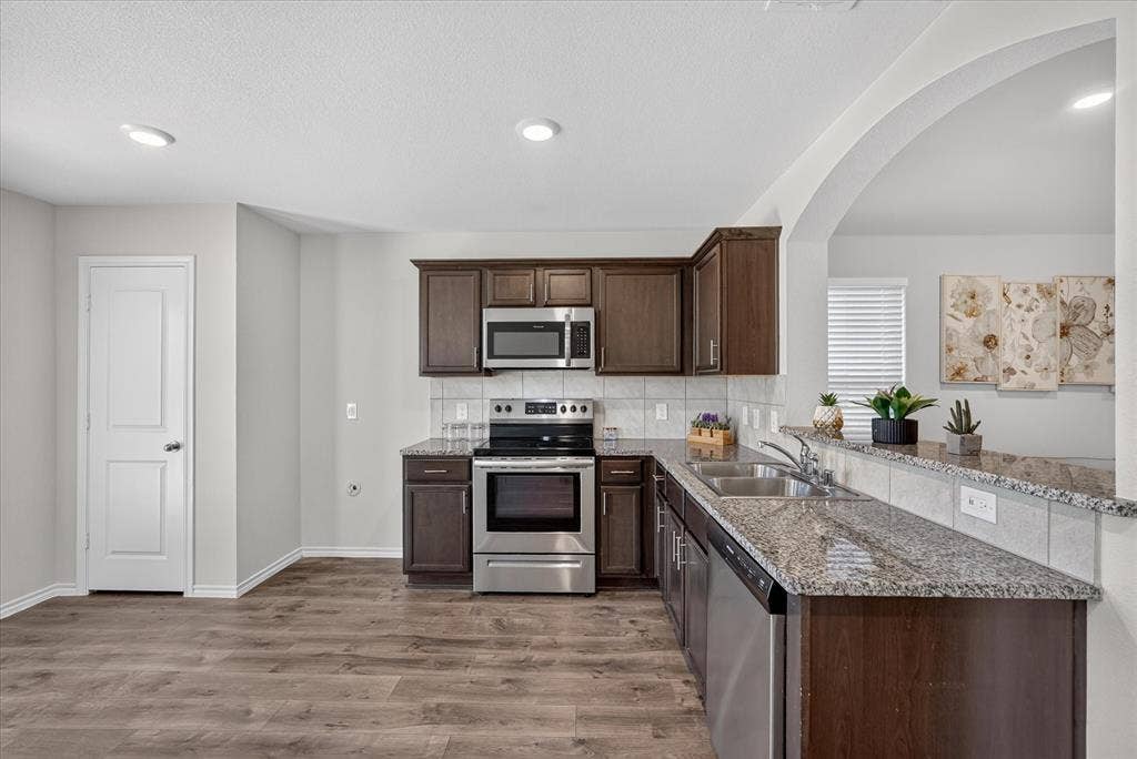 2428 Rosharon Drive, Forney, TX 75126 Wood-finish flooring, dark wood cabinetry, stainless steel appliances, granite countertops, and a subway tile backsplash