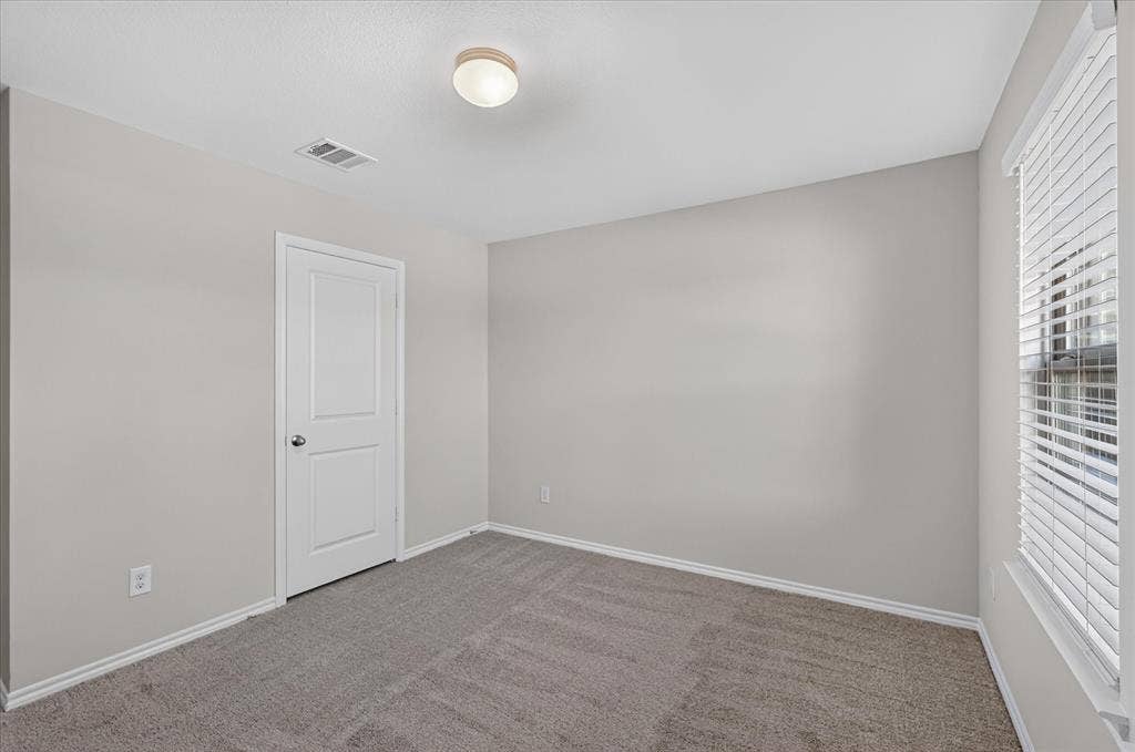 2428 Rosharon Drive, Forney, TX 75126 Spacious bedroom featuring neutral gray walls, plush carpeting, recessed ceiling lighting, and a white six-panel entry door with brushed nickel hardware