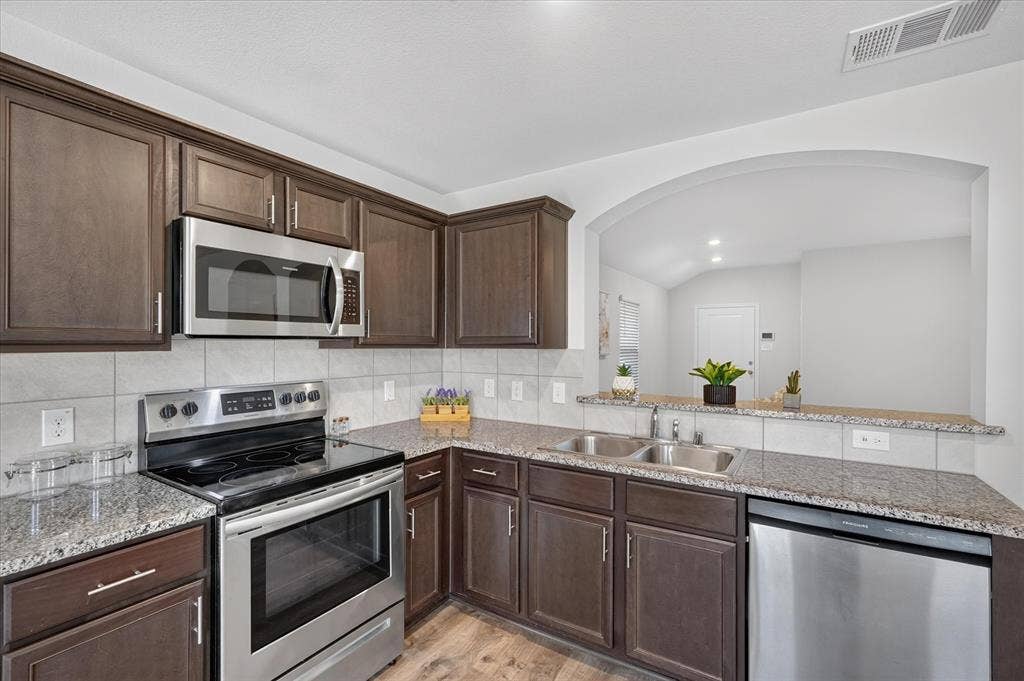 2428 Rosharon Drive, Forney, TX 75126 Kitchen featuring dark wood-finish cabinetry, stainless steel appliances, speckled stone countertops, and a tile backsplash