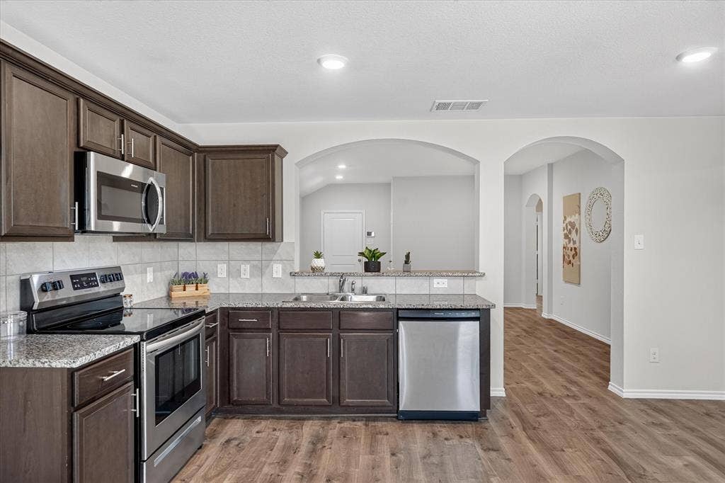 2428 Rosharon Drive, Forney, TX 75126 Kitchen featuring dark wood-finish cabinetry, stainless steel appliances, granite countertops, and a tile backsplash