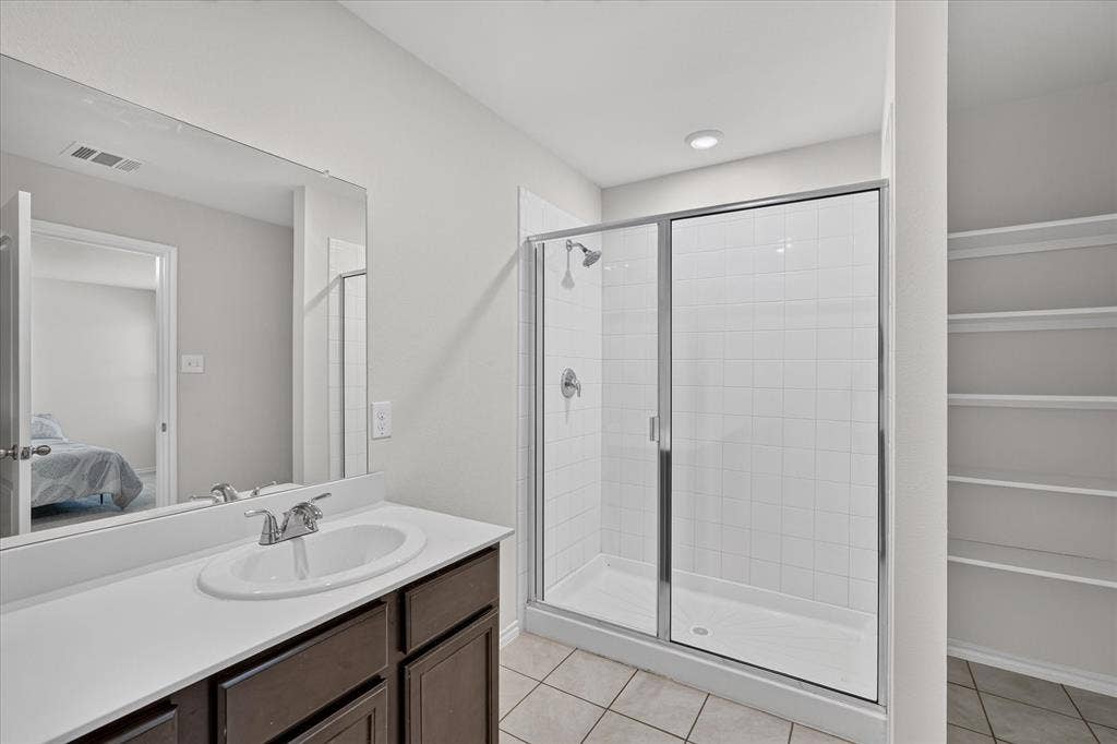 2428 Rosharon Drive, Forney, TX 75126 Spa-inspired primary bathroom featuring a dual-sink vanity with dark wood cabinetry and white quartz countertop, framed mirror with integrated lighting, frameless glass shower enclosure with subway tile surround, chrome fixtures, recessed ceiling lighting, and tile flooring throughout