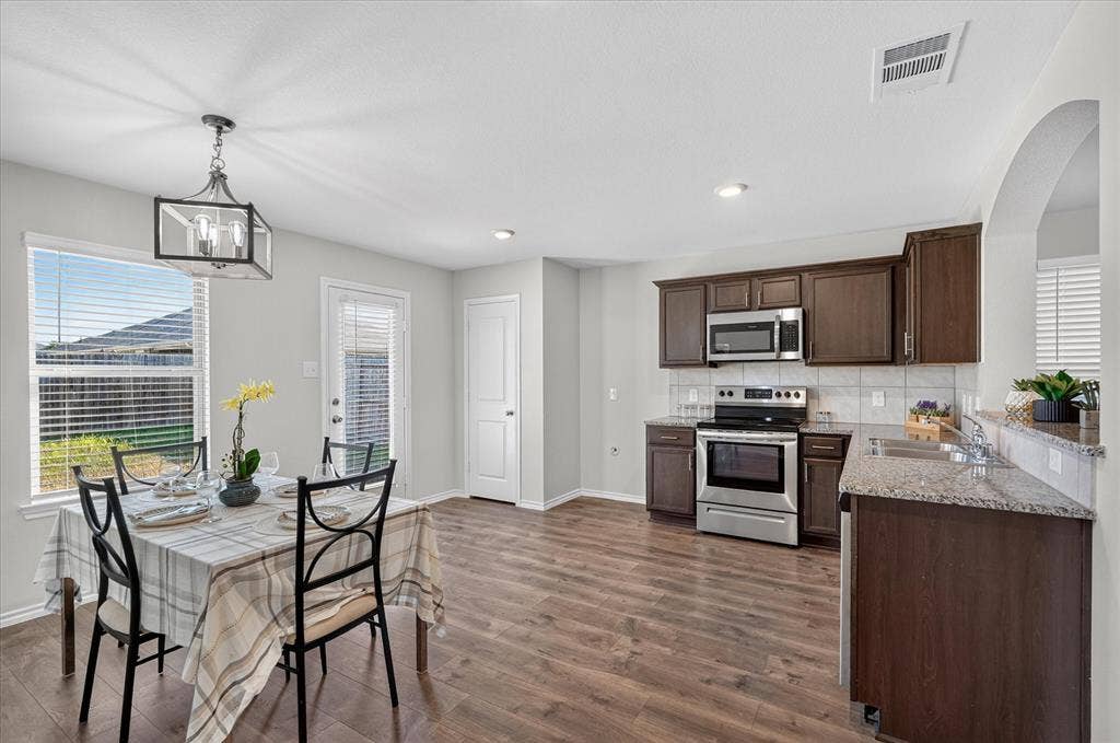 2428 Rosharon Drive, Forney, TX 75126 Spacious kitchen and dining area featuring wood-finish flooring, stainless steel appliances, dark wood cabinetry, and light-toned countertops