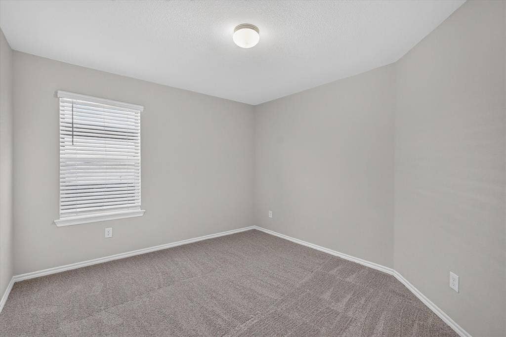 2428 Rosharon Drive, Forney, TX 75126 Bright secondary bedroom featuring neutral wall finishes, new carpet flooring with linear pattern detail, large window with horizontal blinds providing natural light, and recessed ceiling lighting
