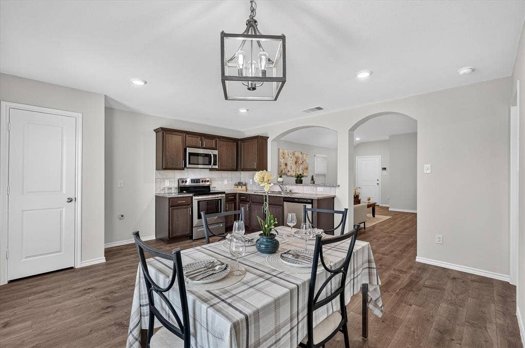 2428 Rosharon Drive, Forney, TX 75126 Open-concept kitchen and dining area featuring wood-finish flooring, dark wood cabinetry, stainless steel appliances, and a white subway tile backsplash