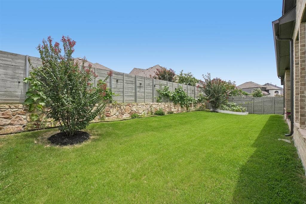 Expansive backyard featuring a manicured lawn, stone retaining wall, and mature landscaping