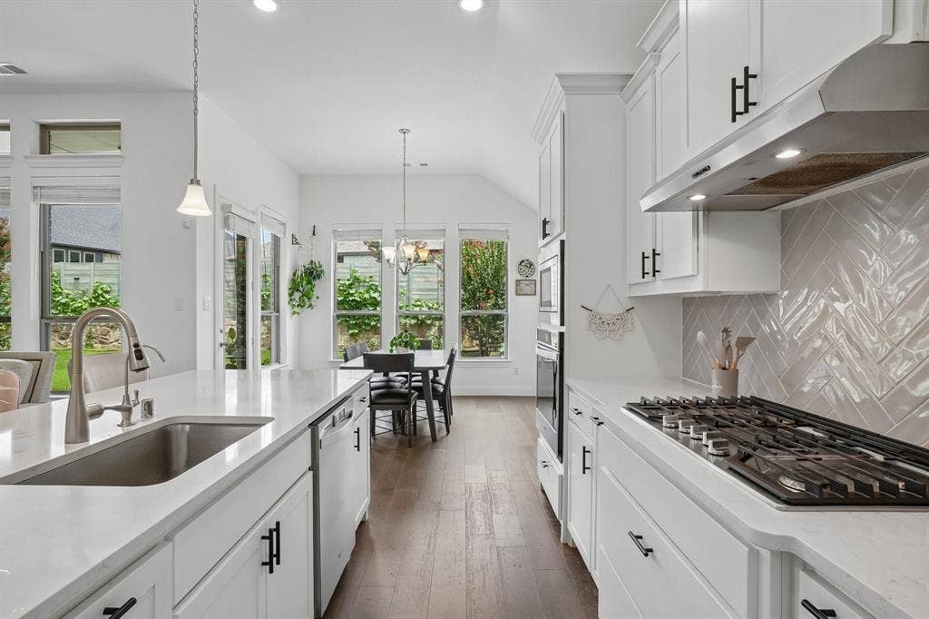 White shaker cabinetry, light-toned countertops, stainless steel sink with a gooseneck faucet, integrated dishwasher, and a herringbone-patterned tile backsplash