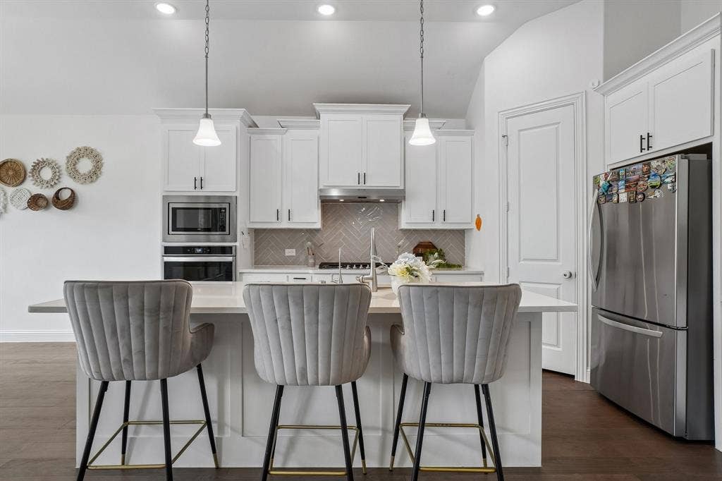 White cabinetry with crown molding, stainless steel appliances, herringbone tile backsplash, kitchen island with seating, and dark wood-finish flooring