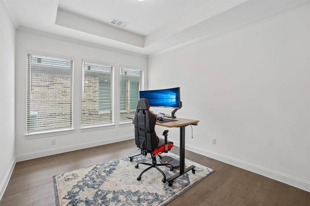 Wood-finish flooring with white baseboards, a tray ceiling, and three windows featuring blinds