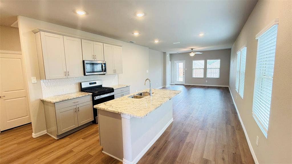 505 Blanton Street, McKinney, TX 75069 Kitchen island with double basin sink, light-toned cabinetry, stainless steel microwave, gas range, and wood-finish flooring throughout