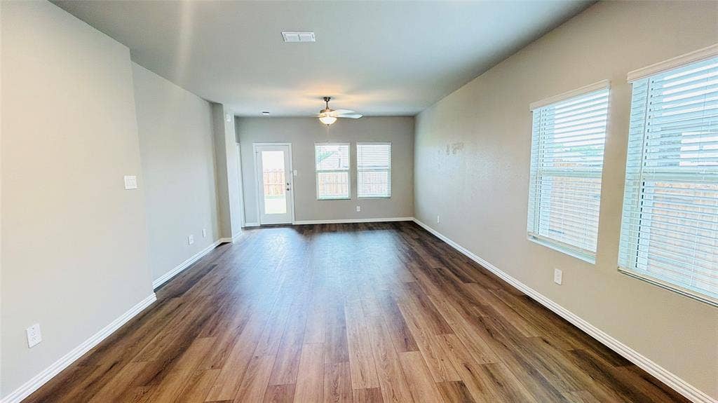 505 Blanton Street, McKinney, TX 75069 Spacious room featuring wood-finish flooring, light neutral walls, multiple windows with blinds, a ceiling fan, and a glass-paneled exterior door