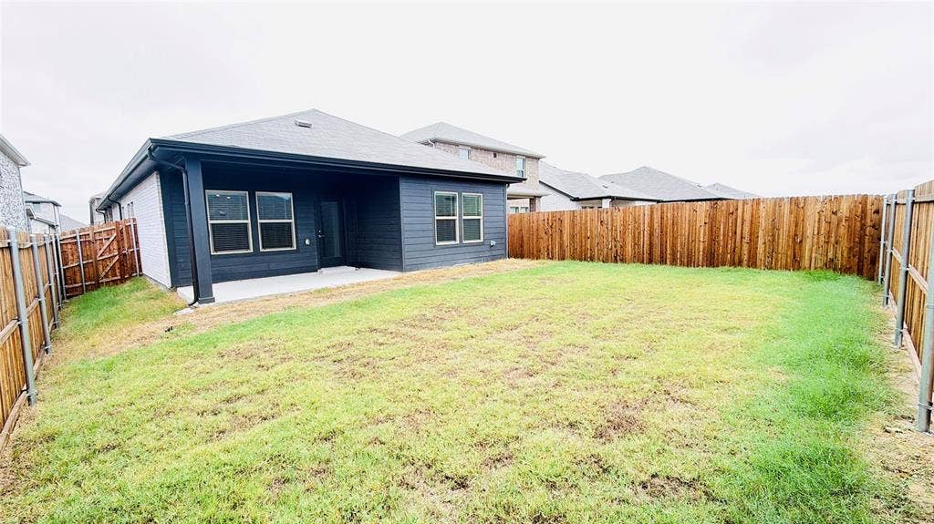 505 Blanton Street, McKinney, TX 75069 Backyard featuring a concrete patio, wood privacy fencing, and a dark-toned exterior with multiple windows