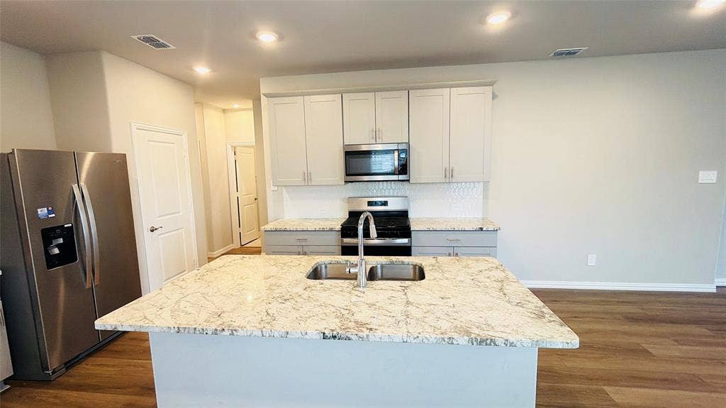 505 Blanton Street, McKinney, TX 75069 Modern kitchen featuring a large island with an undermount sink, stainless steel appliances, light-toned cabinetry, and wood-finish flooring