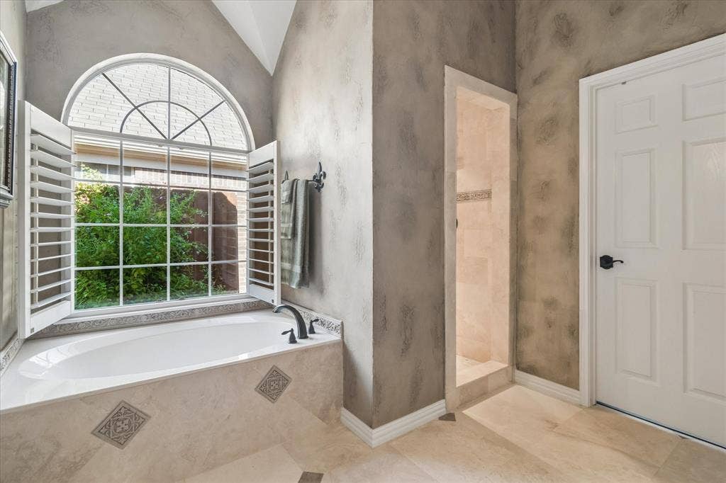 10521 Chablis Lane, Frisco, TX 75035 Soaking tub with a black faucet, large arched window, window shutters, tiled shower, and a paneled door