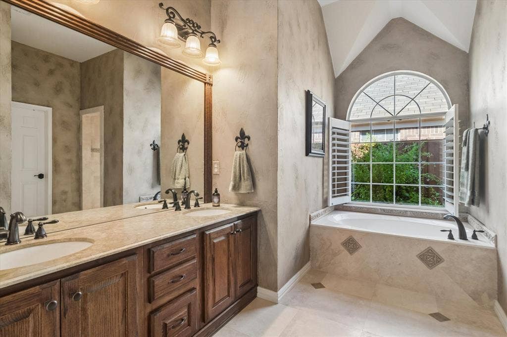 10521 Chablis Lane, Frisco, TX 75035 Dual vanity with integrated sinks, a large framed mirror, and a built-in garden tub with an arched window