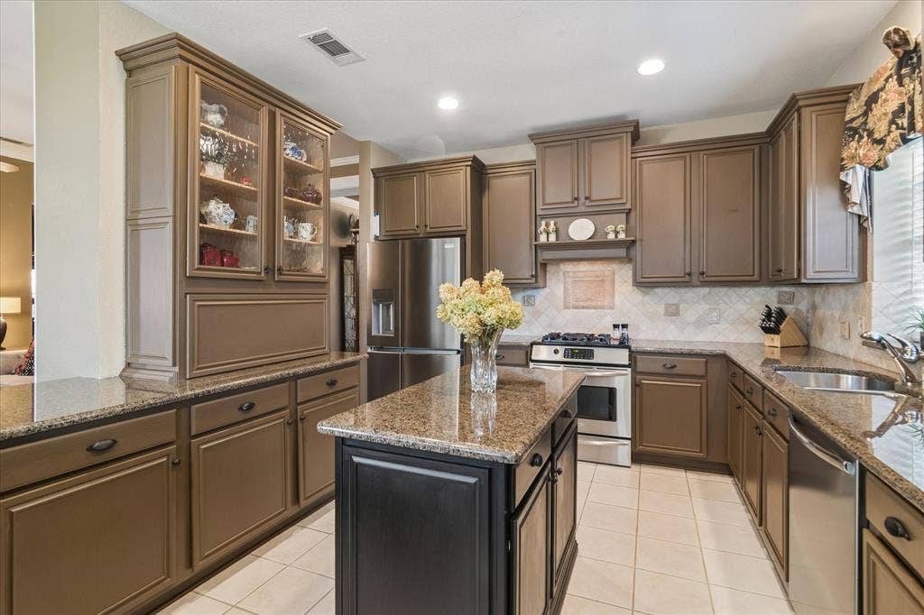 10521 Chablis Lane, Frisco, TX 75035 Expansive kitchen featuring a central island, stainless steel appliances, abundant cabinetry, speckled countertops, and a tiled backsplash