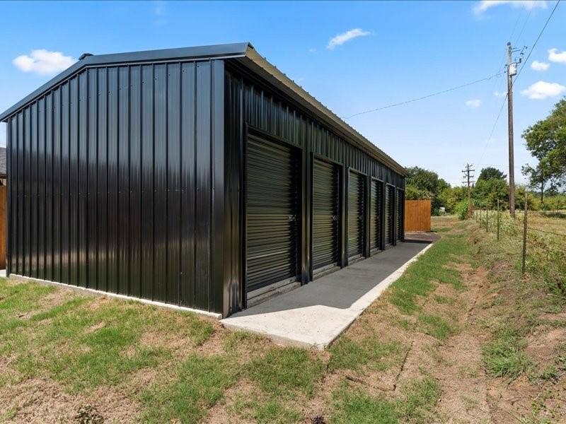 900 S Tool, #12, Tool, TX 75143 STORAGE available on property. Black corrugated metal siding with multiple roll-up doors and a concrete walkway