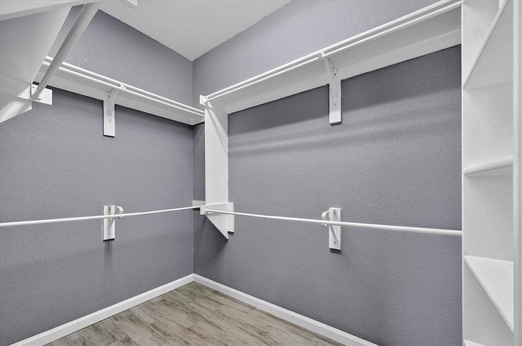 209 Northridge Drive, Wylie, TX 75098 Spacious walk-in closet featuring dual track lighting systems, white metal rod infrastructure, multiple hanging levels, and wood-finish flooring throughout