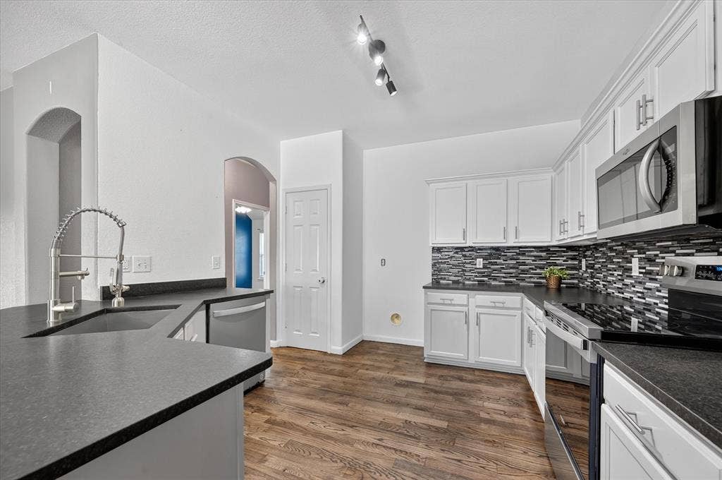 209 Northridge Drive, Wylie, TX 75098 Kitchen featuring white cabinetry, dark countertops, a mosaic tile backsplash, stainless steel appliances, and wood-finish flooring
