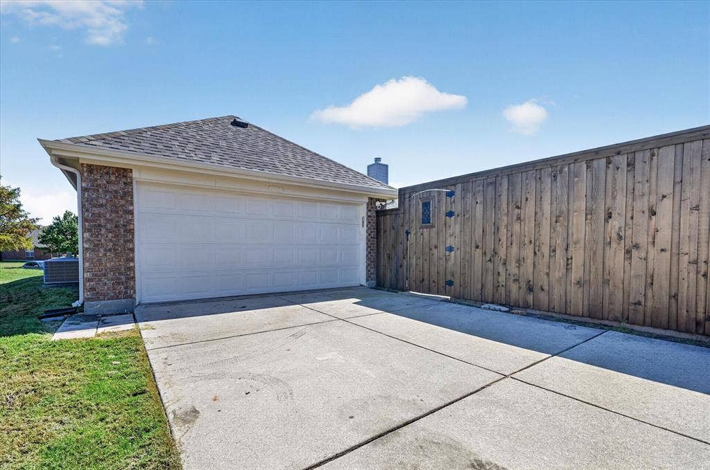 209 Northridge Drive, Wylie, TX 75098 Attached two-car garage with a concrete driveway, brick exterior, and a wood privacy fence featuring an integrated decorative gate