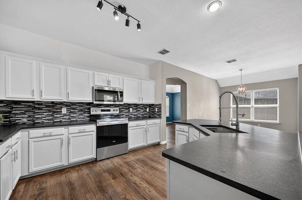 209 Northridge Drive, Wylie, TX 75098 Kitchen featuring white cabinetry, dark countertops, a mosaic tile backsplash, stainless steel appliances, and wood-finish flooring