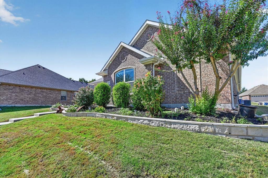 209 Northridge Drive, Wylie, TX 75098 Brick exterior with arched window, concrete walkway, and landscaping featuring mature trees and shrubs
